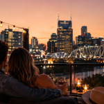 Millennial couple enjoying a romantic rooftop evening overlooking the Nashville skyline at sunset with city lights, candles, and live music vibes.