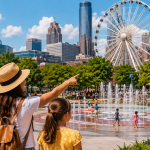 Family of four enjoying Atlanta attractions near Centennial Olympic Park with views of the Georgia Aquarium, SkyView Ferris wheel, World of Coca-Cola, fountains, and downtown skyline on a sunny day.